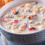 Creamy seafood soup with mixed shellfish and potatoes in a blue ceramic bowl, ready to serve
