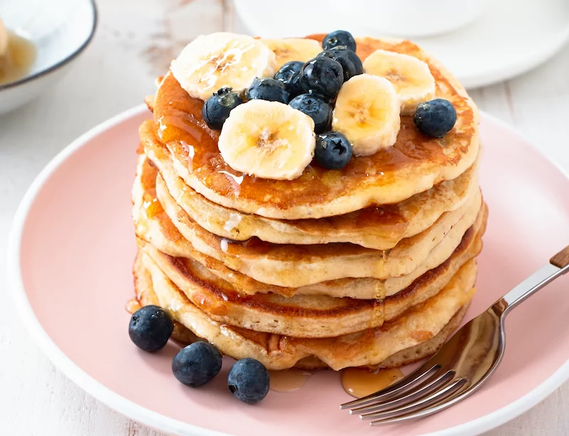 a stack of protein pancakes on a plate topped with bananas and blueberries