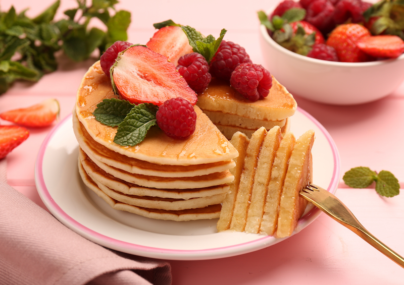 a stack of protein pancakes topped with strawberries on a pink plate