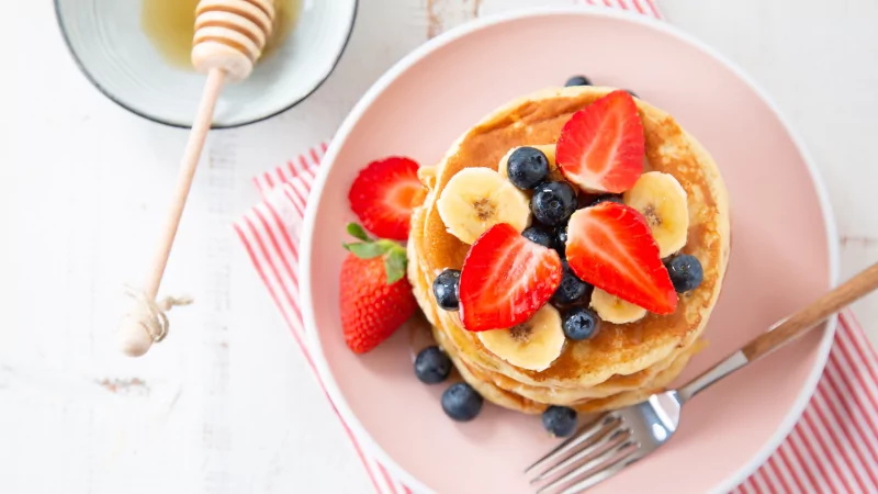 a flatlay of protein pancakes, fruit, and honey