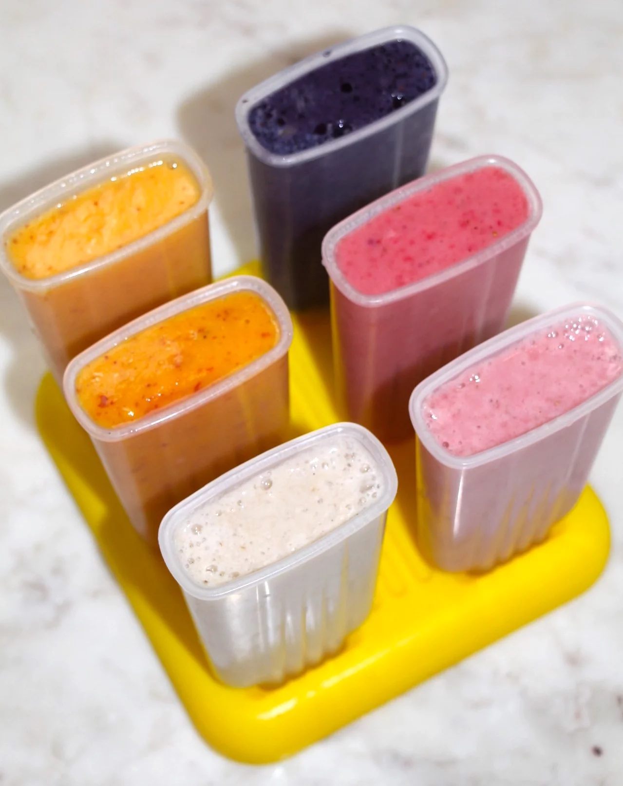 6 different Fresh Fruit Popsicles in molds on a countertop