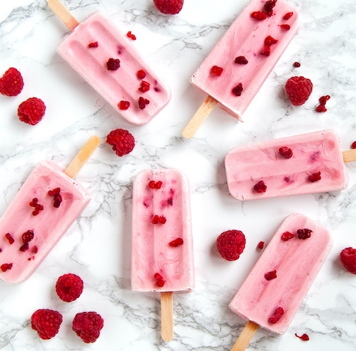 6 popsicles and raspberries on a kitchen countertop