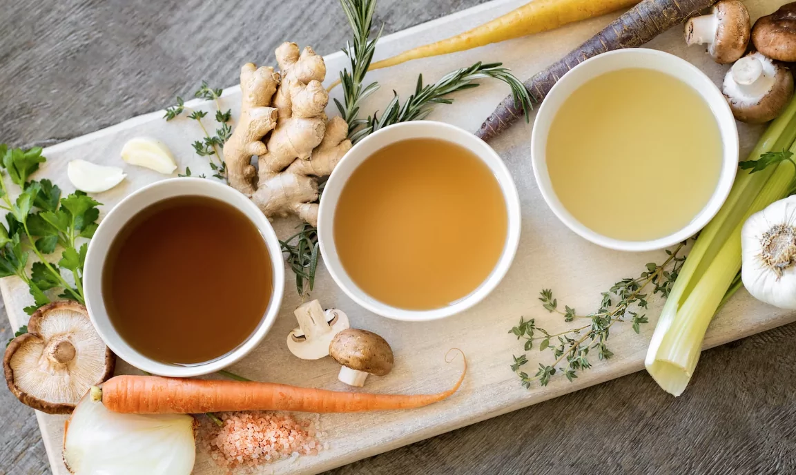 different broths, herbs, carrots, and soup ingredients on a cutting board