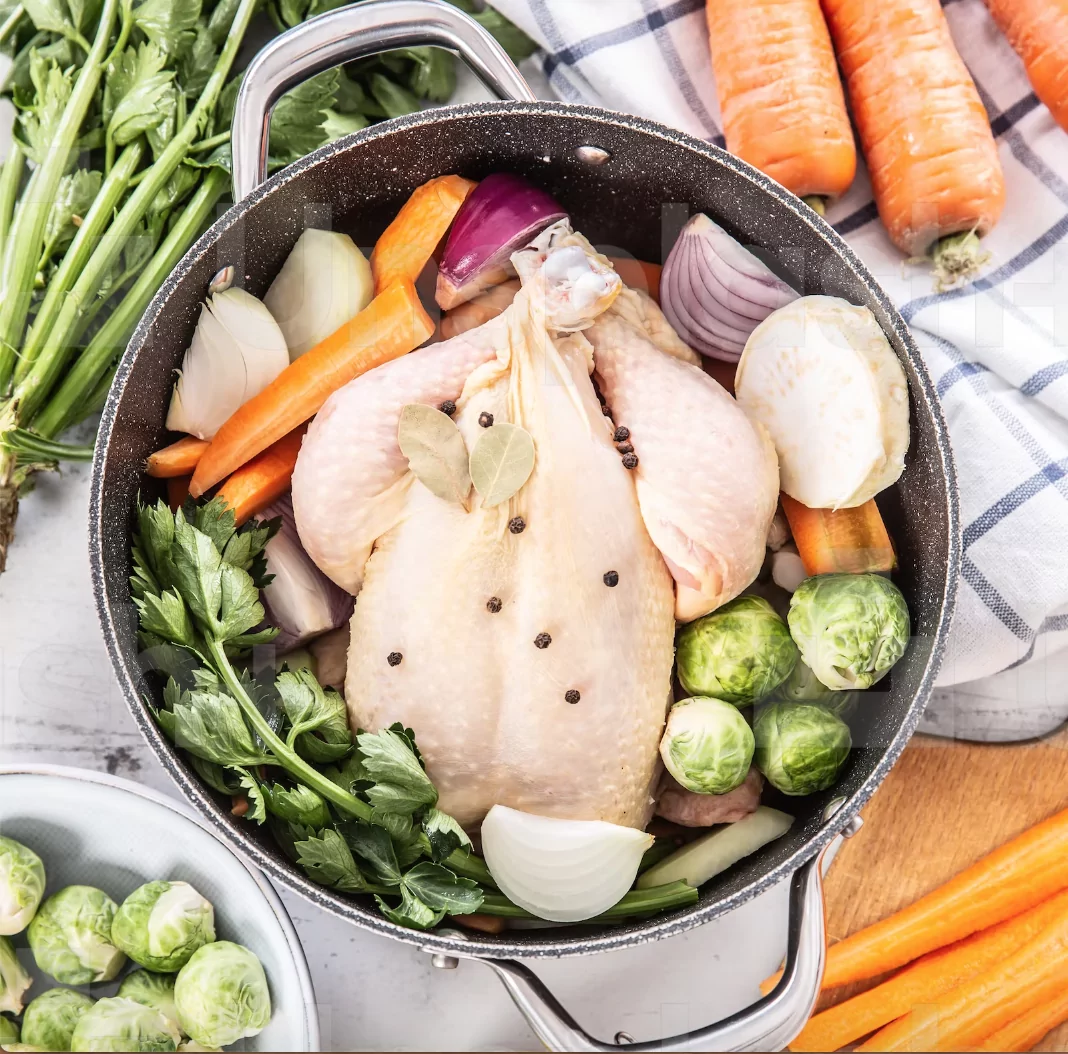 a chicken in a pot with different soup vegetables