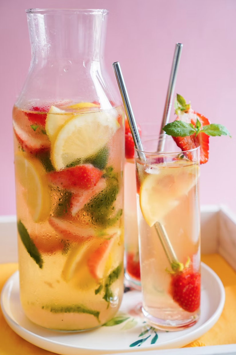 a pitcher and glass of water with fresh fruit and mint on a table