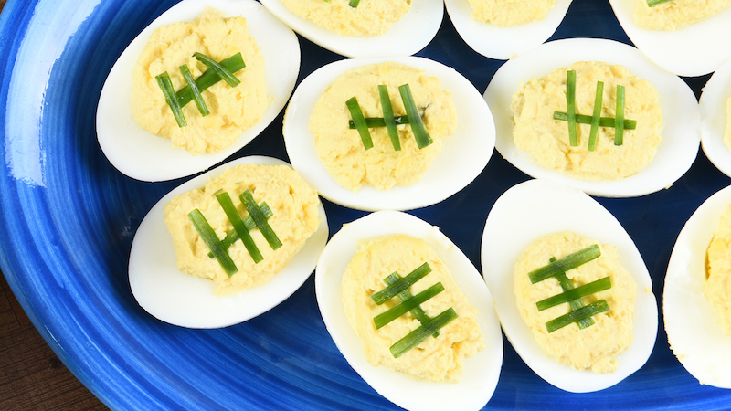 deviled eggs with green onions to make them look like footballs on a blue platter