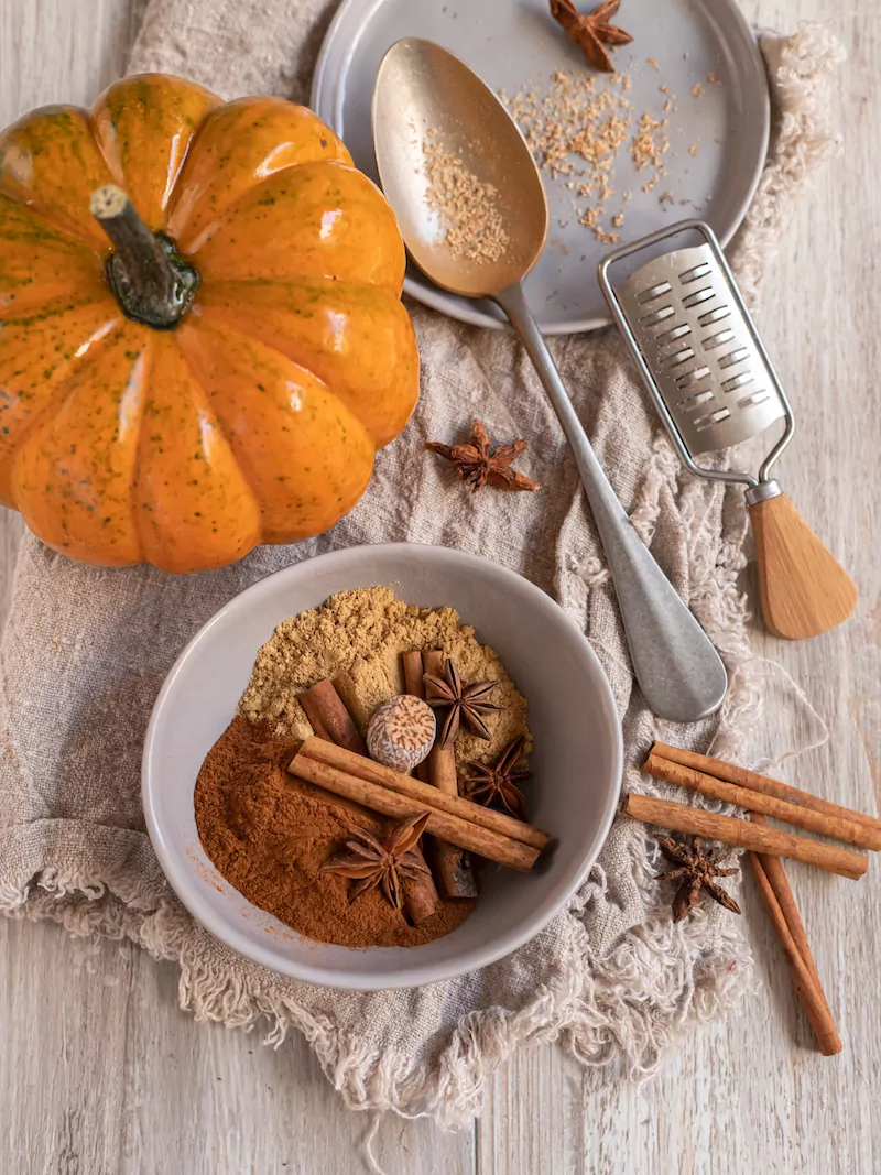 pumpkin spice a mini pumpkin, cinnamon sticks, and pumpkin spice ingredients in a bowl on a wooden surface