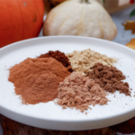 5 spices that make pumpkin spice in a bowl next to mini pumpkins