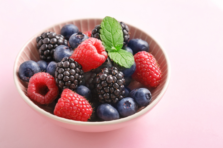a bowl of berries with liqueur a bowl of mixed berries topped with mint and liqueur on a pink surface