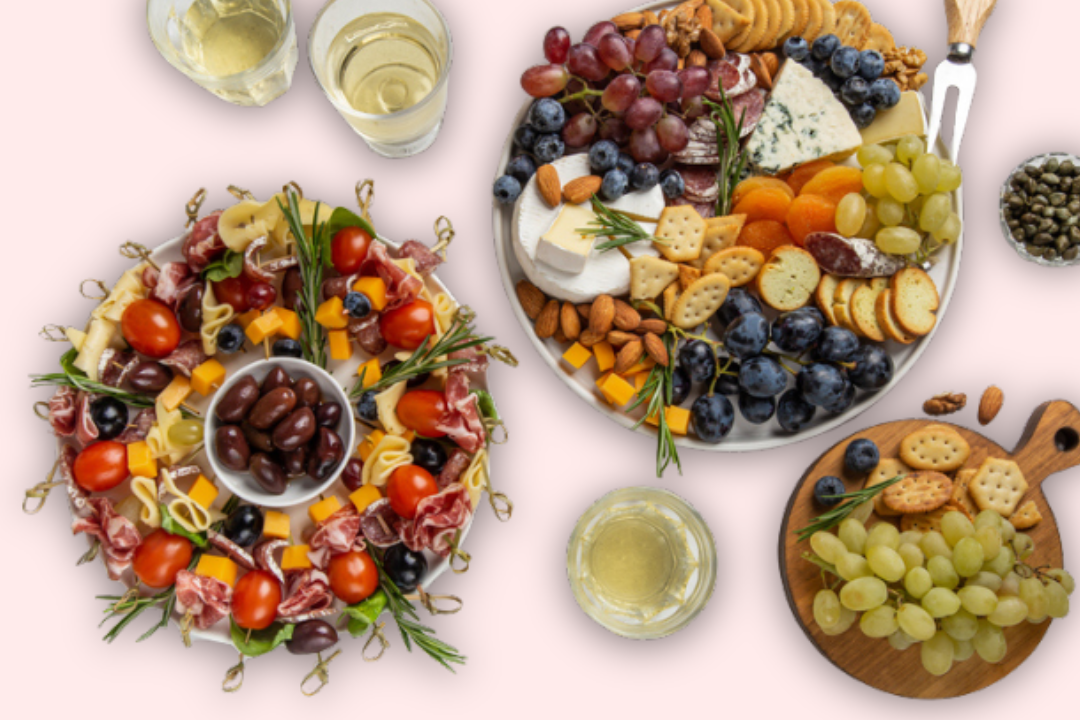 Charcuterie Board a flat lay of two charcuterie boards topped with various fruits, cheeses, meats, vegetables, nuts, crackers, and glasses of wine