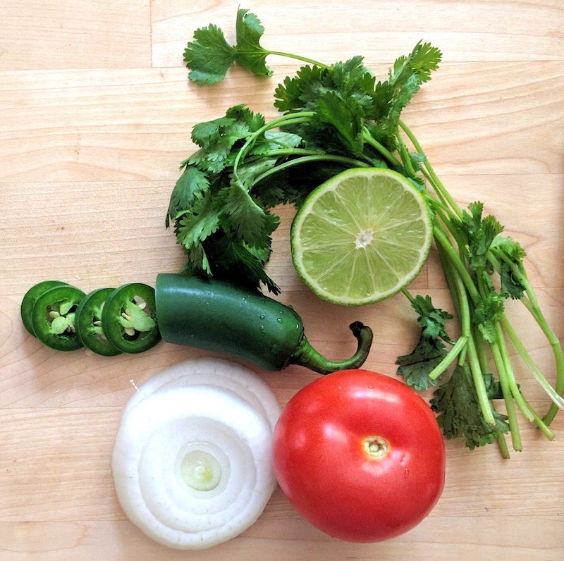 cilantro, lime, jalapeno, tomato, and onion on a cutting board
