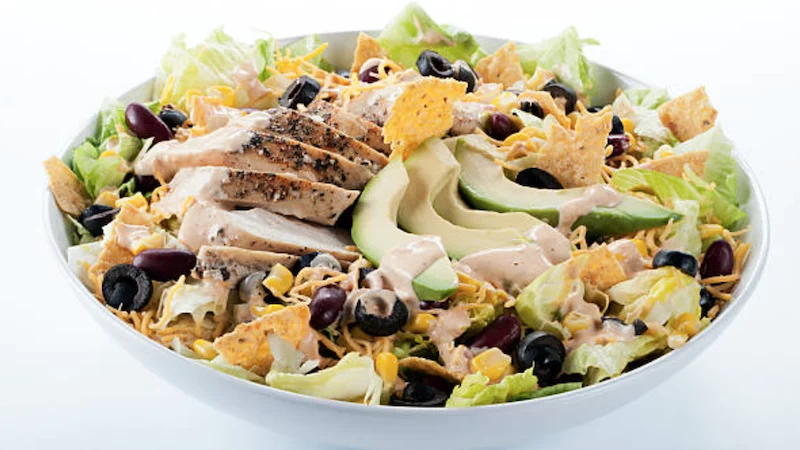 a bowl with lettuce, black olives, grilled chicken, avocado, tortilla chips, and cheese
