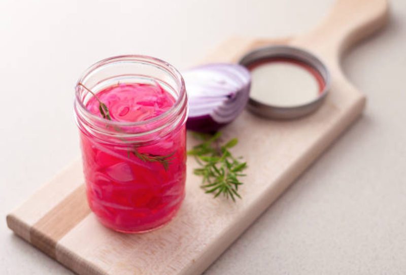 Pickled red onions in a jar on a cutting board