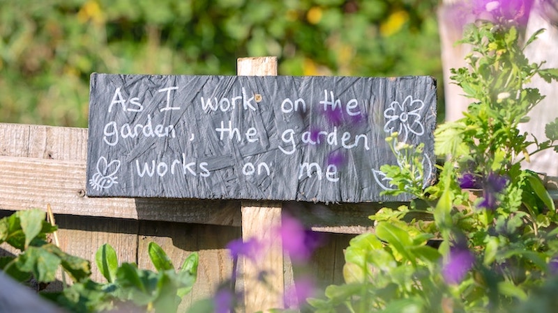 A garden sign that says "As I work on the garden, the garden works on me."