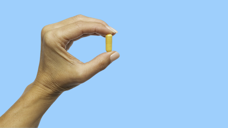 a hand holding a berberine pill for cravings on a blue background