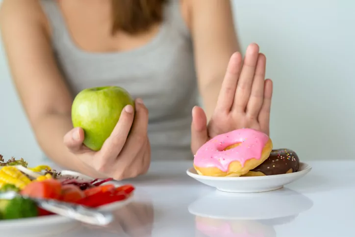 Young woman rejecting Junk food or unhealthy food such as donut or dessert and choosing healthy food such as fresh fruit or vegetable.