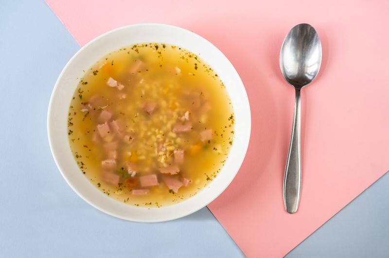 a bowl of soup and a spoon on a pastel background
