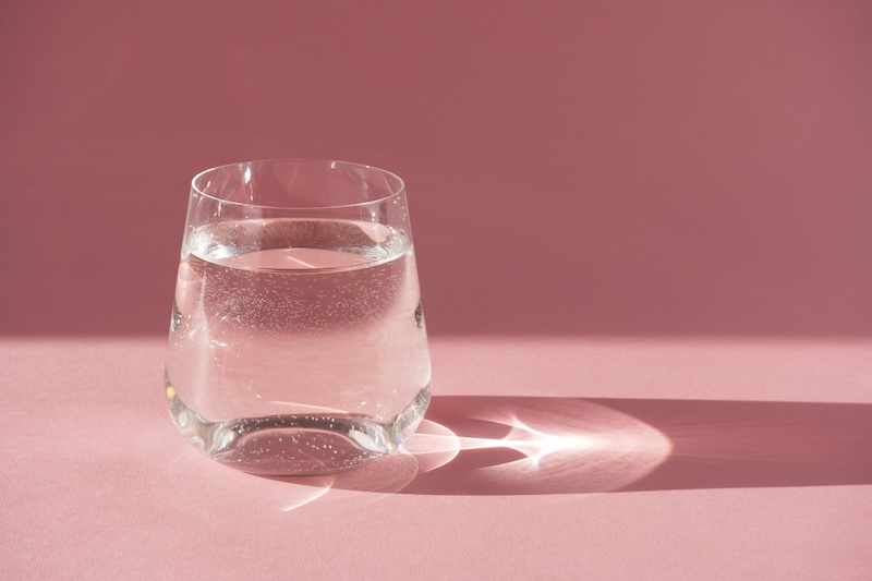 a glass of water on a pink background