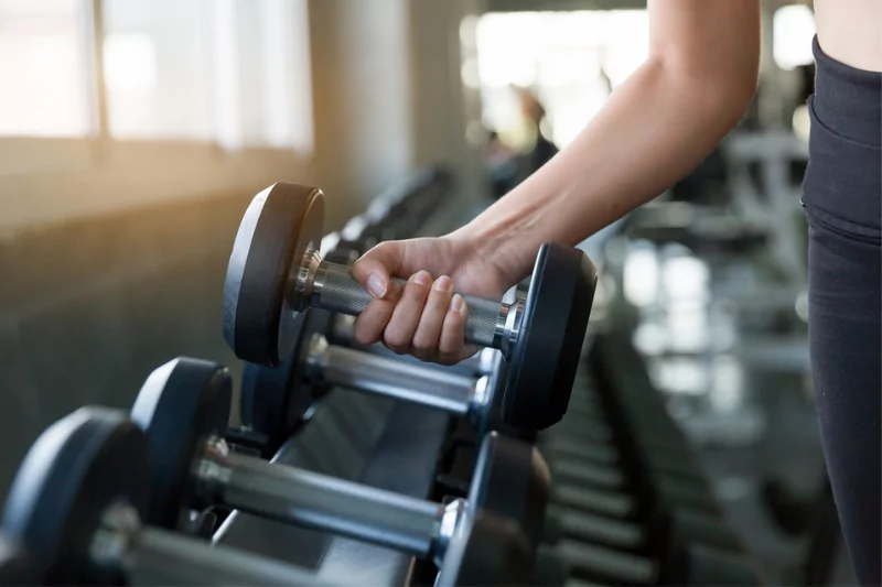 a woman's arm grabbing a dumbbell off a weight rack