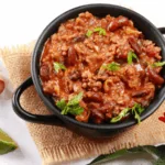 Bowl of healthy chili made with organic ground beef and red kidney beans, topped with cilantro, surrounded by lime, garlic, and chili peppers — an easy one-pot high-protein chili recipe by Dr. Christina Carlyle.