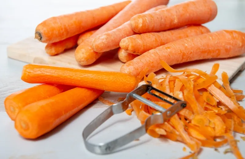 Carrot Salad raw carrots on a cutting board a peeler and peeled carrots