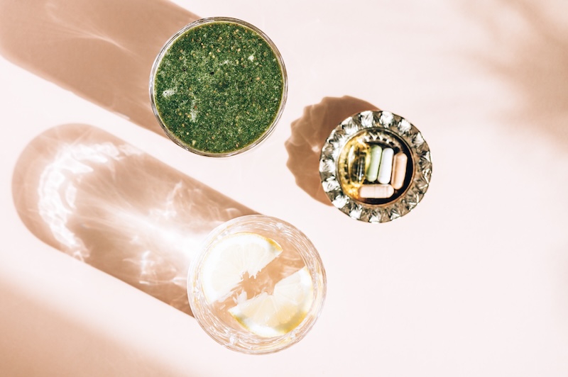 Healthy Green ULT Shake, Glass of water with lemon and bunch of daily supplements nearby. Strong shadows from the sun. Healthy summer breakfast, top view