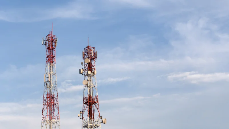 Two tall red and white EMF and cellular communication towers against a blue sky, representing electromagnetic field exposure and potential health concerns