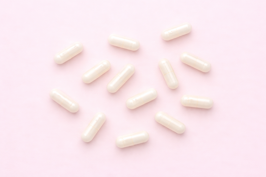 Flat lay of white DAO supplement capsules arranged on a soft pink background, representing diamine oxidase supplements used to support histamine breakdown and histamine intolerance.