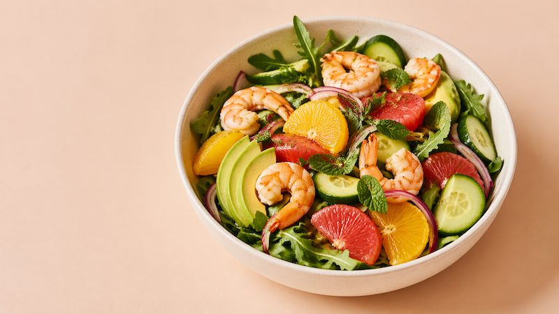 Citrus shrimp summer salad with grapefruit, orange, avocado, cucumber, and red onion in a white bowl on a beige background
