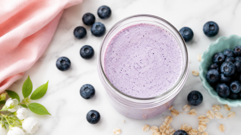 Vanilla Blueberry Antioxidant Smoothie Vanilla blueberry breakfast smoothie in a glass jar with fresh blueberries, oats, and soft pink and aqua styling on a white marble background.